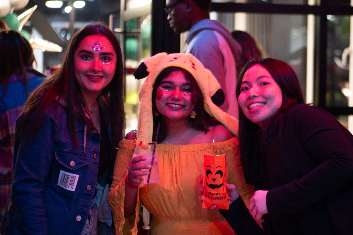 Three students pose with Halloween popcorn and a Pikachu hat