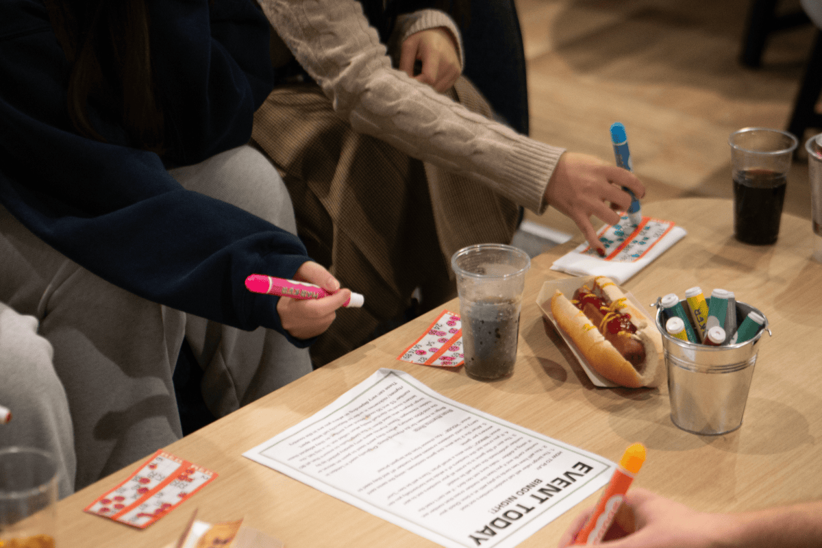 Students marking bingo cards and eating a delicious hot dog placed on the table