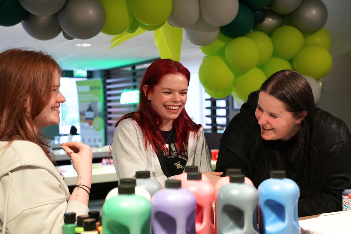 Three friends laughing together at the code sip and paint event