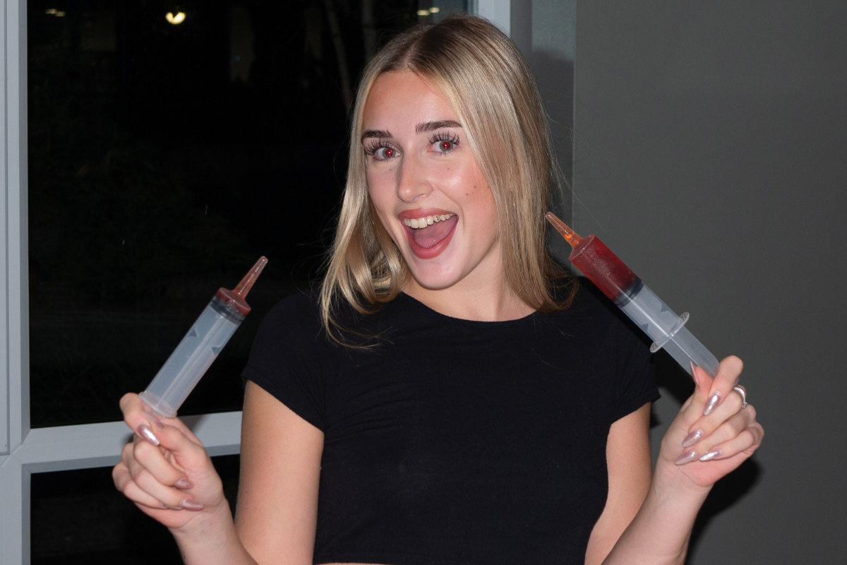 A girl holding up two syringes filled with shots