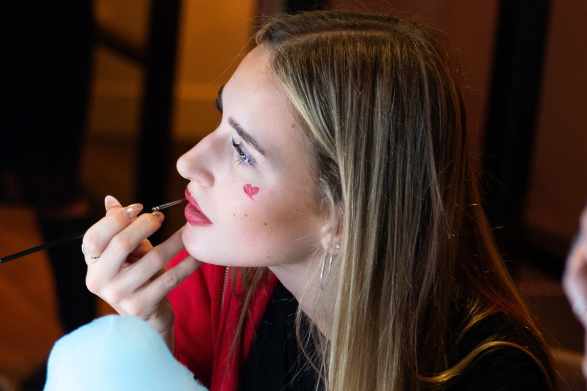 A girl painting her lips read at the face paint station at the CODE Halloween event