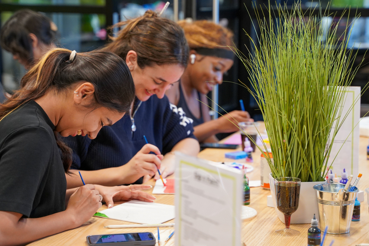 Three students smiling whilst focusing on painted masterpieces