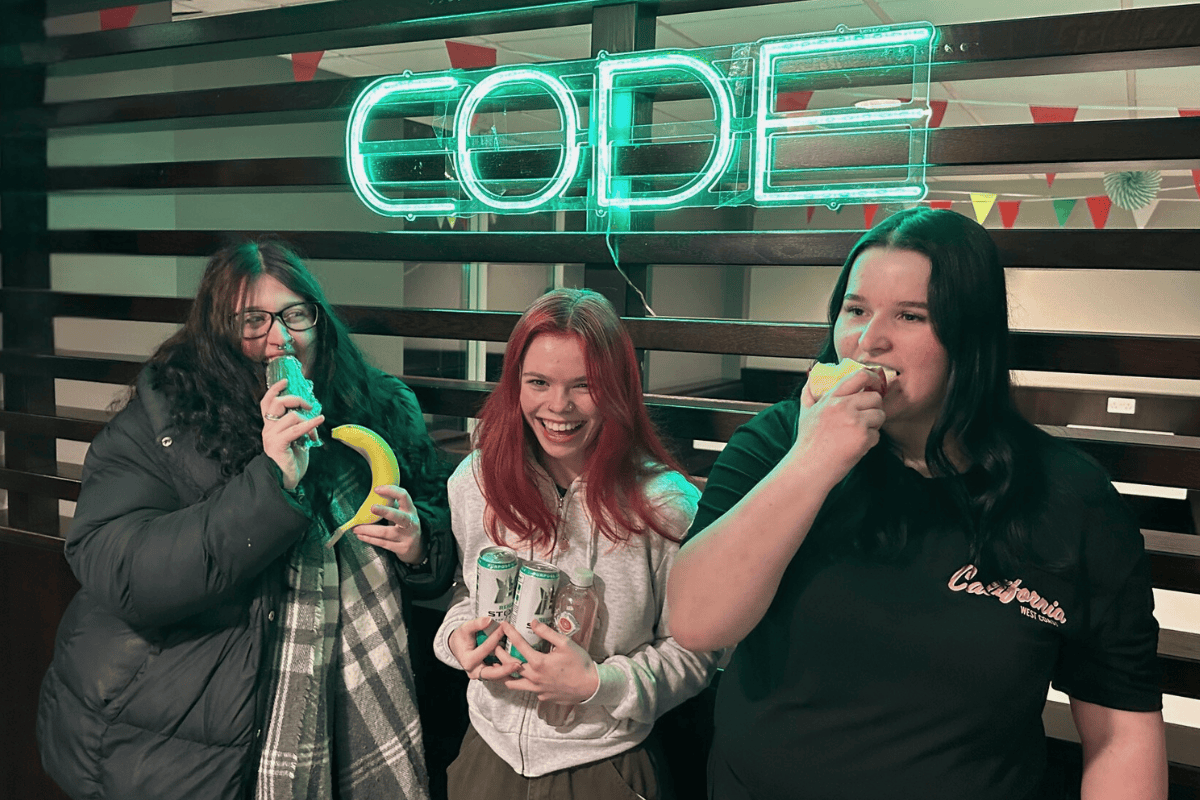 Three friends posing in front of the CODE sign with their fruit and veg