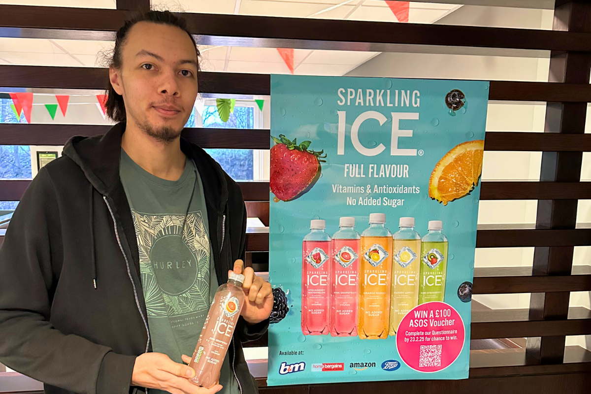 a guy posing with a vitamin water by the sign