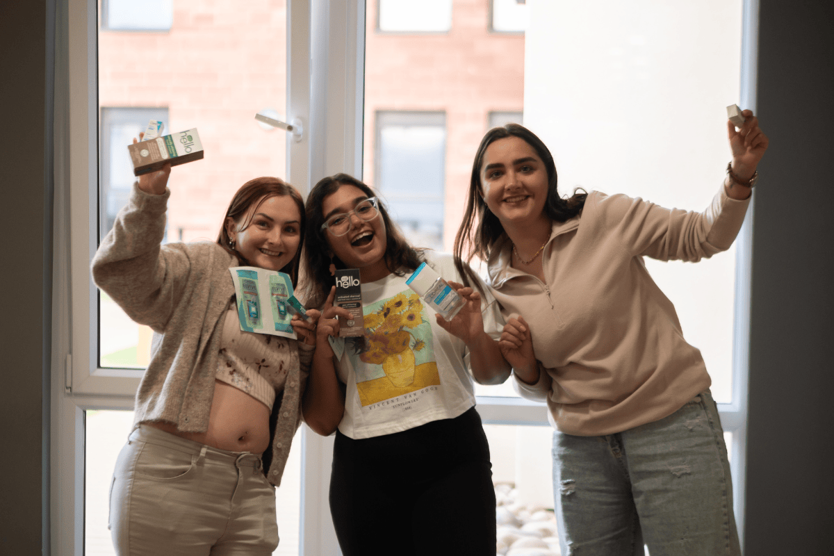 Three students smiling holding up Pamper products