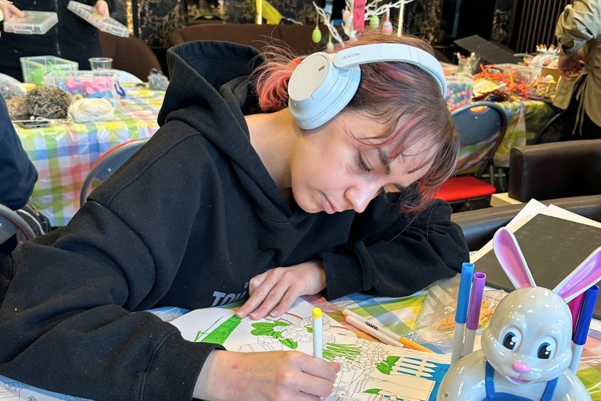 A girl with headphones on, doing some colouring in at the code event