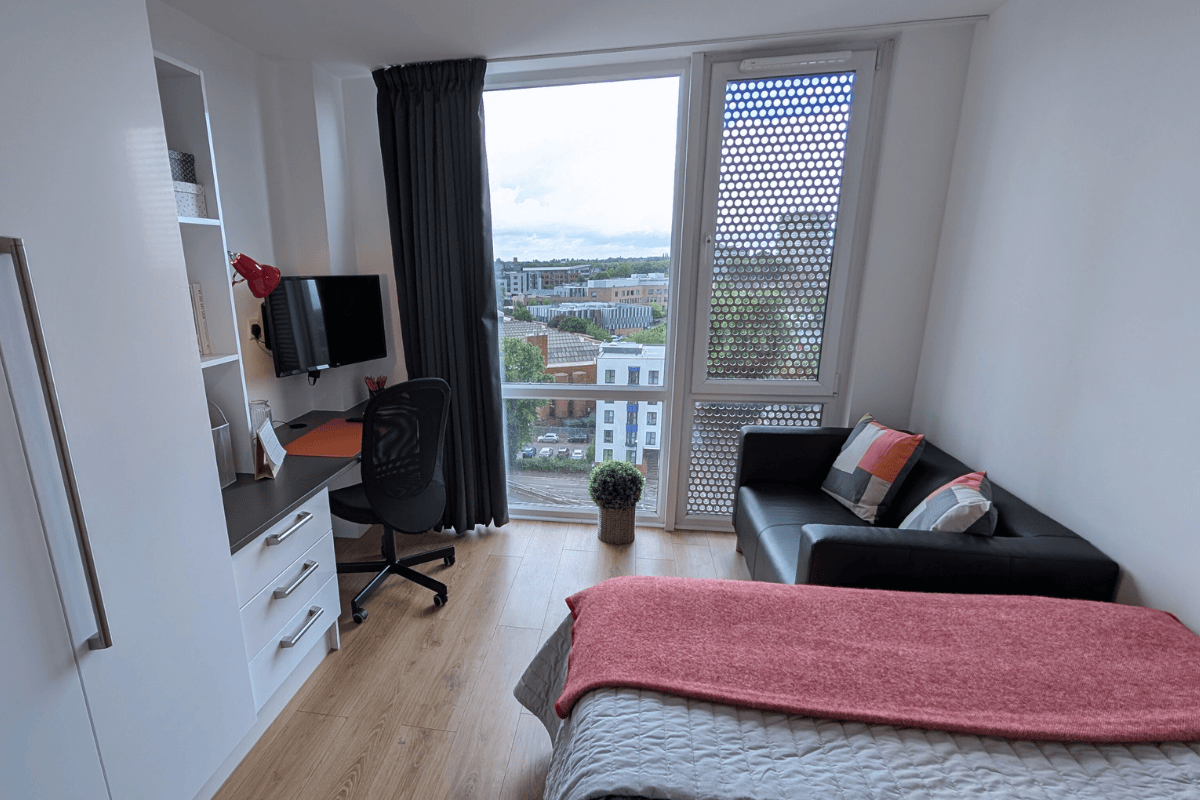 Bed and desk facing a large floor to ceiling window in a 10th Floor Studio