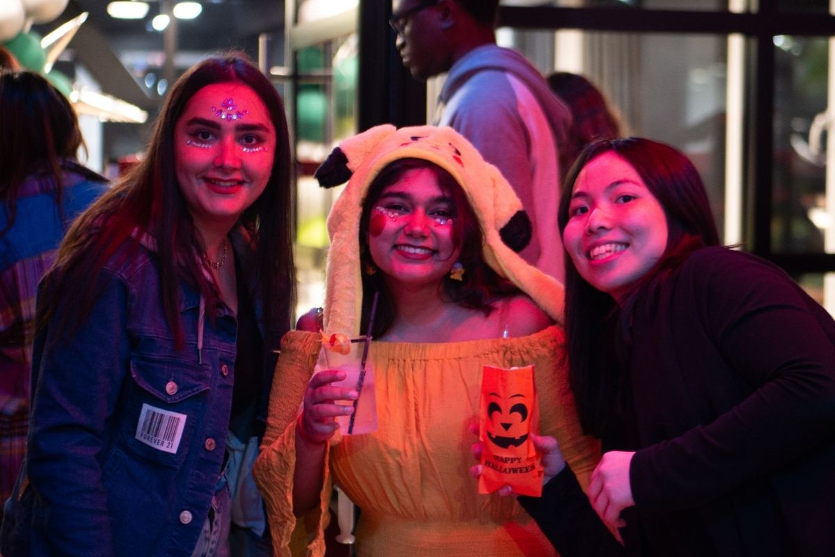 Three students pose with Halloween popcorn and a Pikachu hat