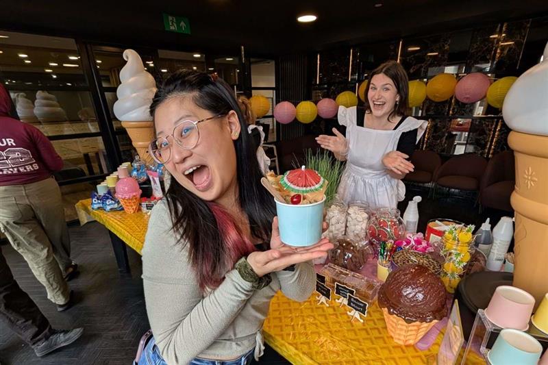 A tenant holding her ice cream cup at the CODE ice cream event with a CODE team member in the background attending the ice cream table