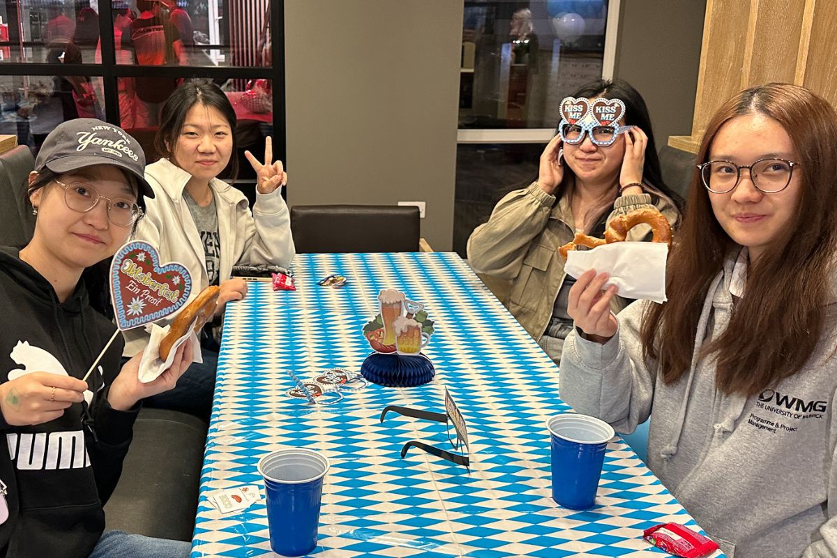 Students hold up a giant pretzel and Oktoberfest masks